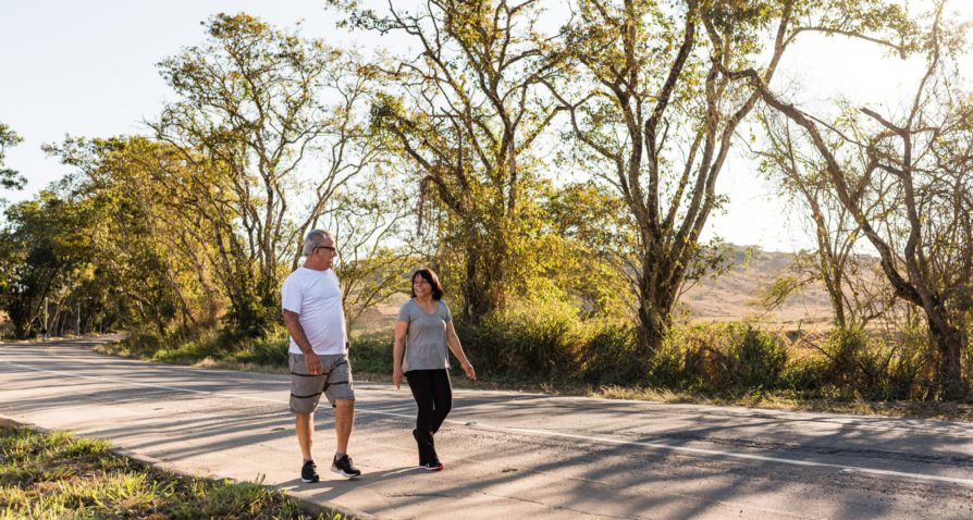 Senior couple walking outdoors on a sunny day, surrounded by trees and nature. They are engaged in a pleasant conversation, representing a healthy and active lifestyle. This image is related to the topic of when to enroll in a Medicare plan, emphasizing the importance of timely health coverage decisions for an active senior life.