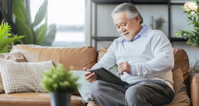 old asian senior grandfather enjoy sunday weekend reading notebook on sofa couch at home,home isolation senior male adult relax casual happiness at home